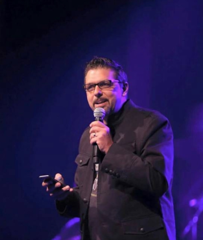 A man in glasses and a jacket is holding a microphone